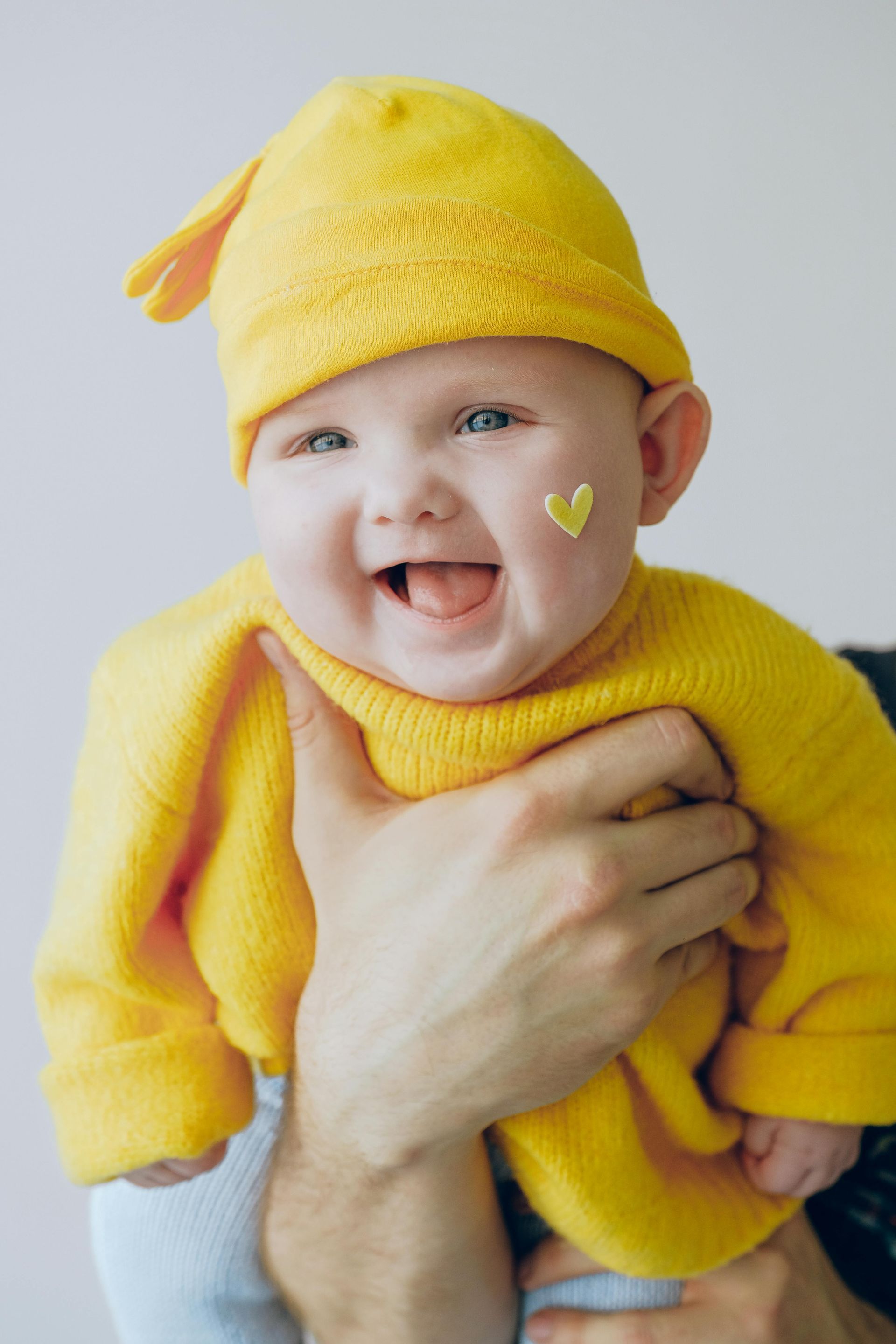 A baby wearing a yellow hat and sweater is being held by a person.