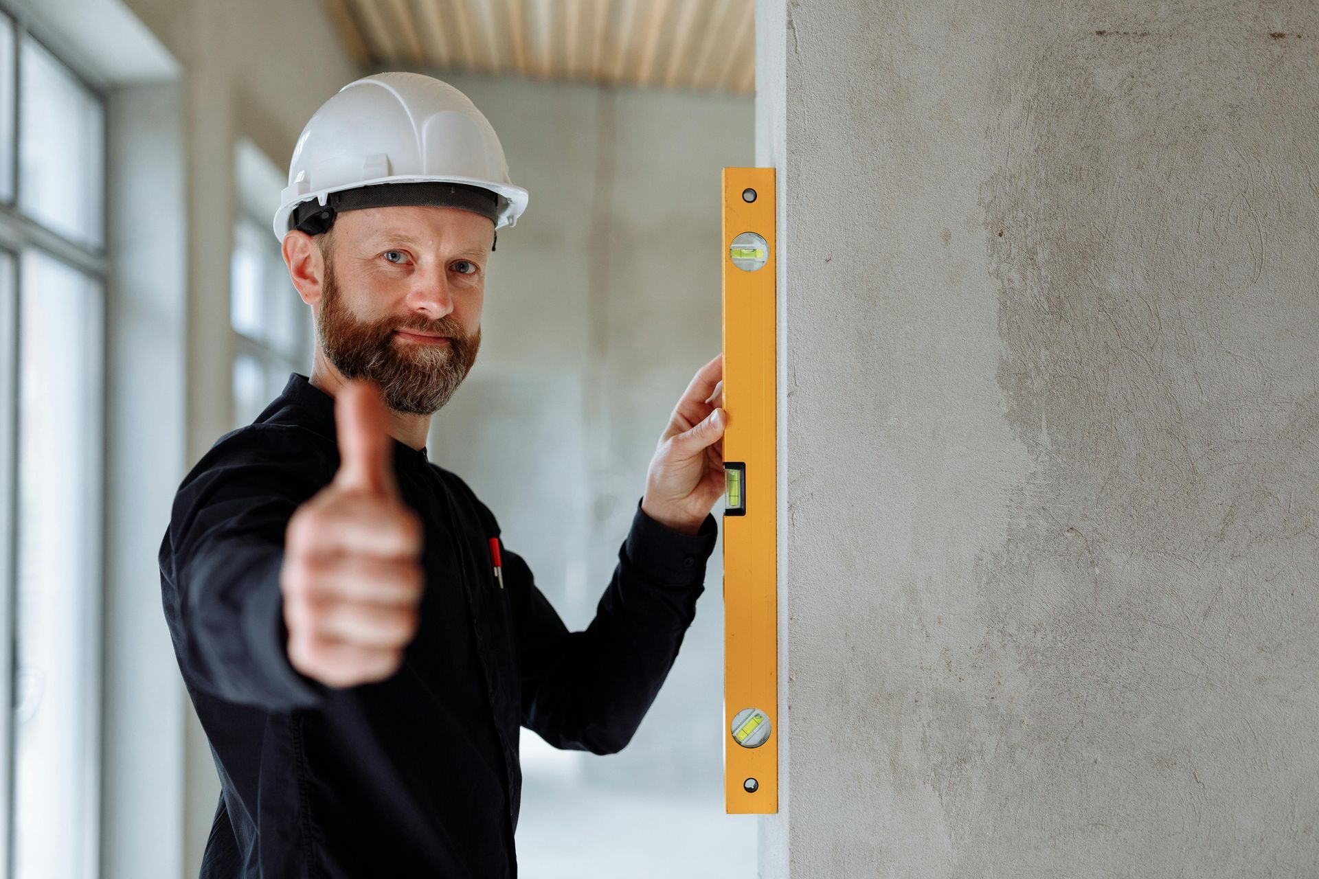 A man is holding a level on a wall and giving a thumbs up.