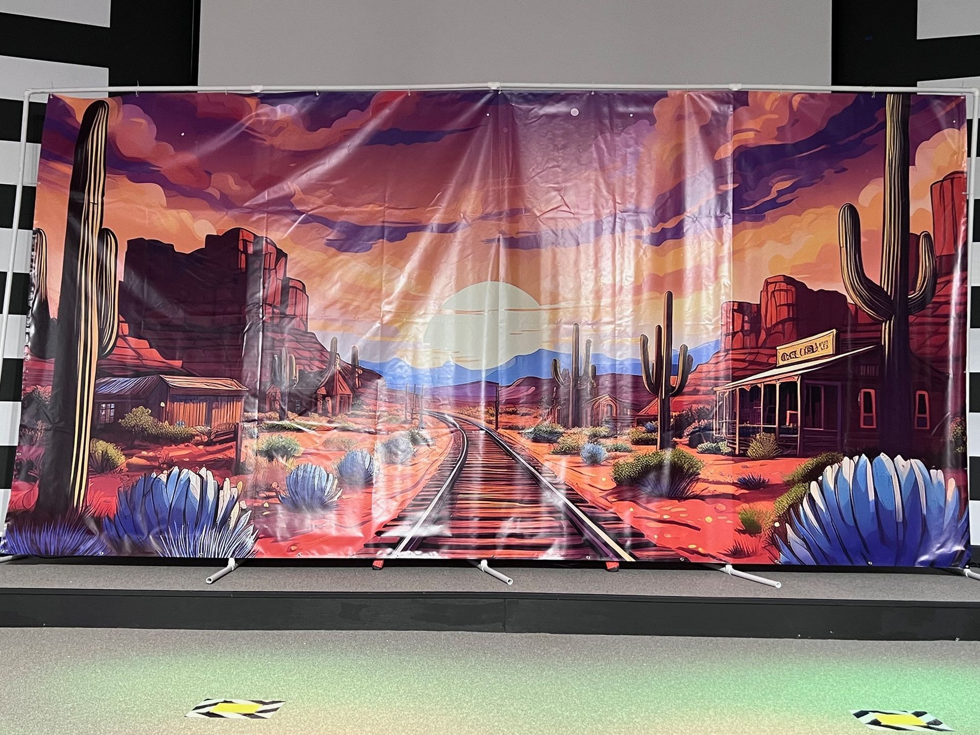 A large painting of a desert with train tracks and cactus.