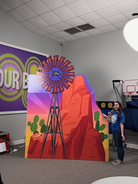 A woman stands in front of a painting of a windmill in front of a sign that says 