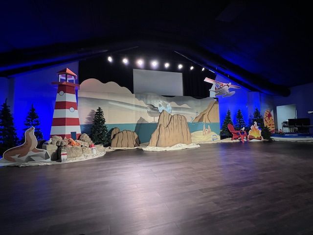 A stage with a lighthouse , seals , mountains and trees on it.