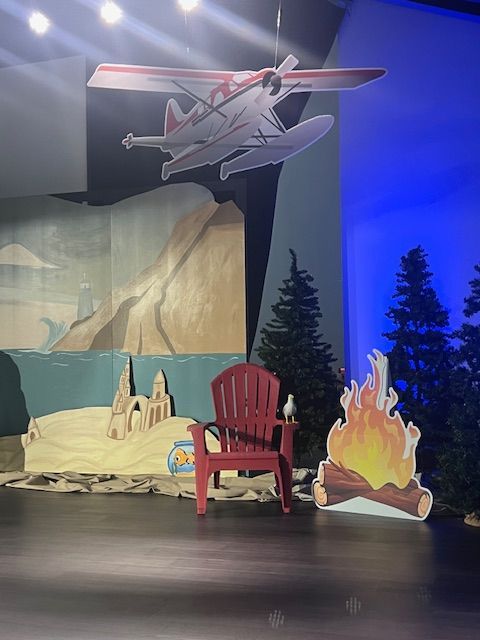 A red chair is sitting on a stage with a seaplane hanging from the ceiling above it