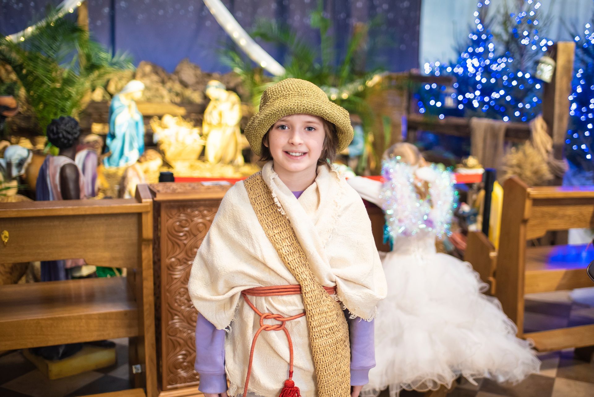A little girl in a nativity scene costume is standing in front of a nativity scene.