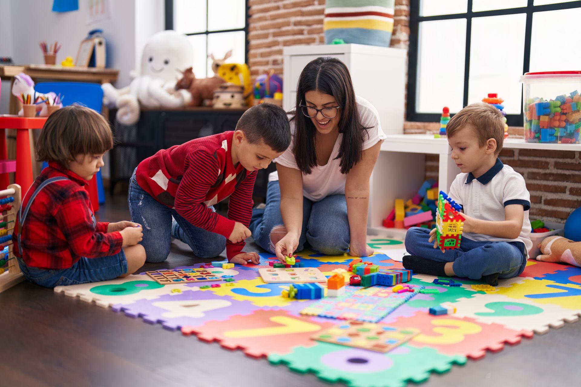 A woman is sitting on the floor with three children playing with toys.