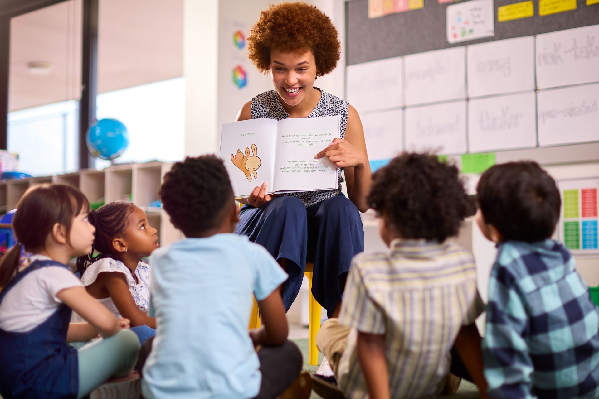 A teacher is reading a book to a group of children in a classroom.