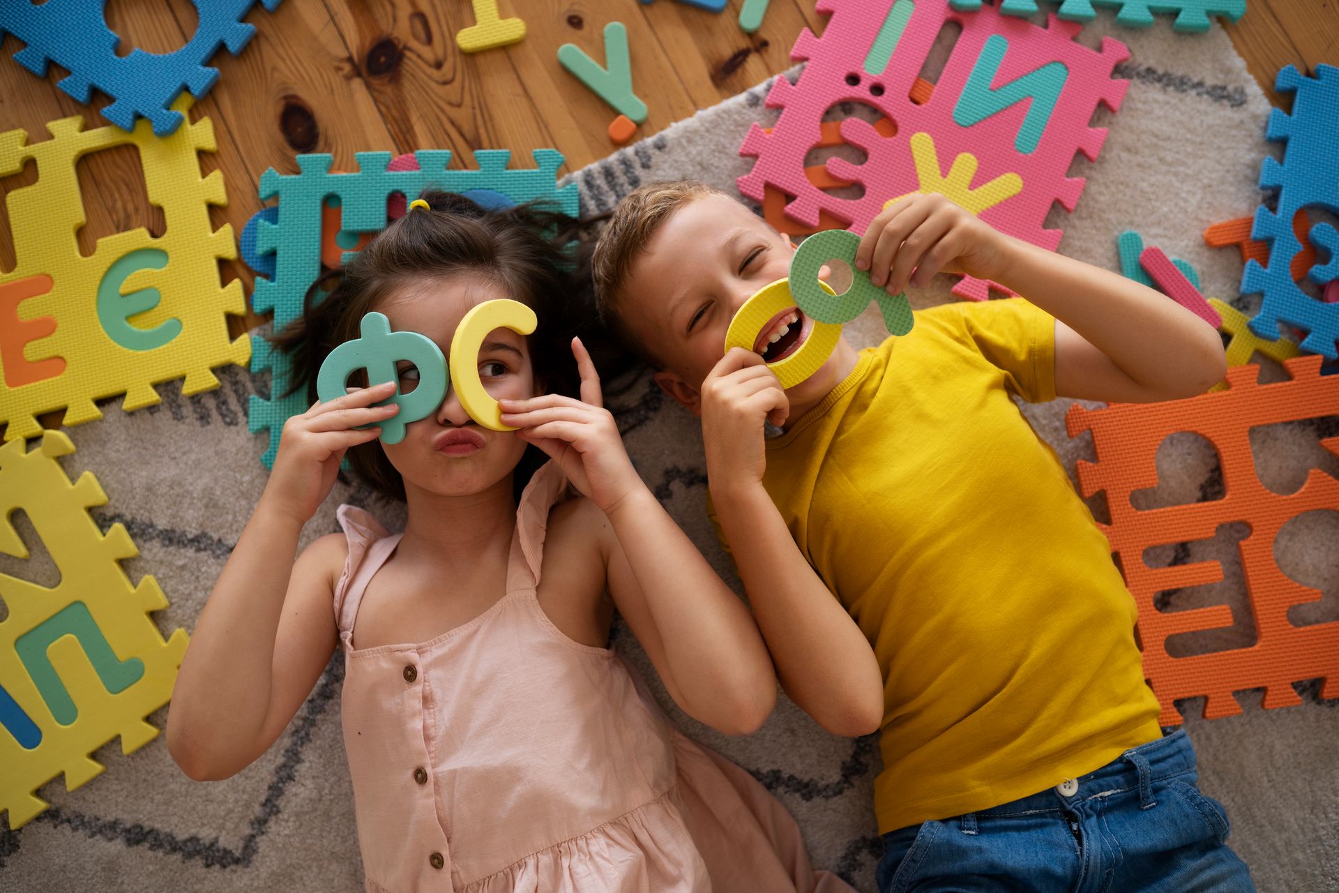A boy and a girl are laying on the floor playing with puzzle letters.