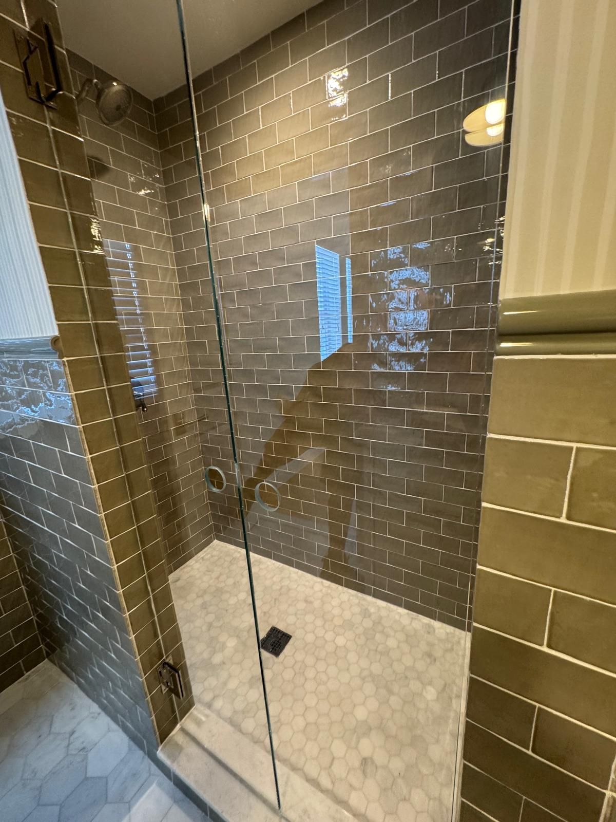 A modern shower with dark green subway tile walls, a clear glass door, and a white tiled floor.