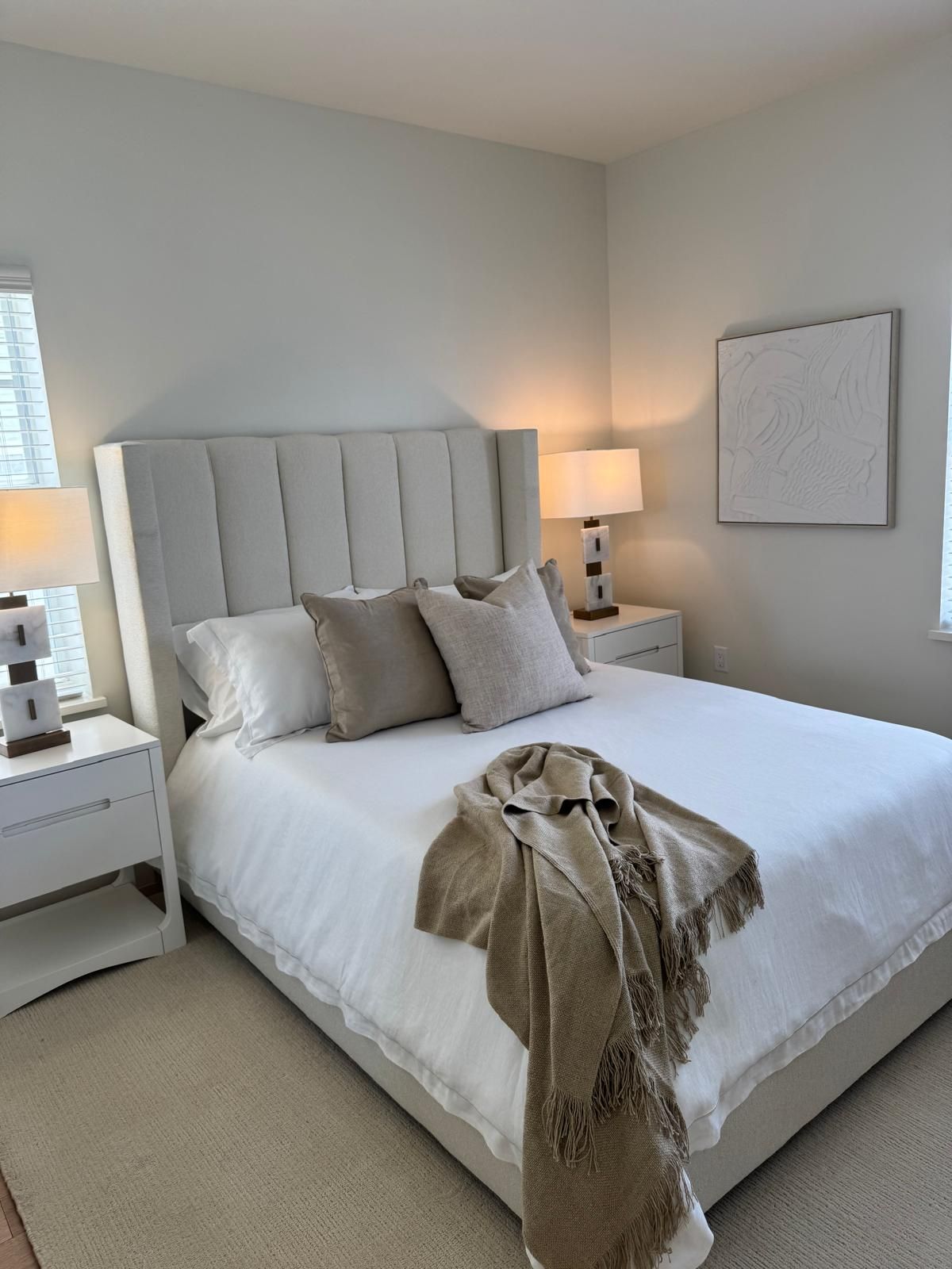 Bedroom with a bed, nightstands, lamps, beige accents, and a neutral color palette.