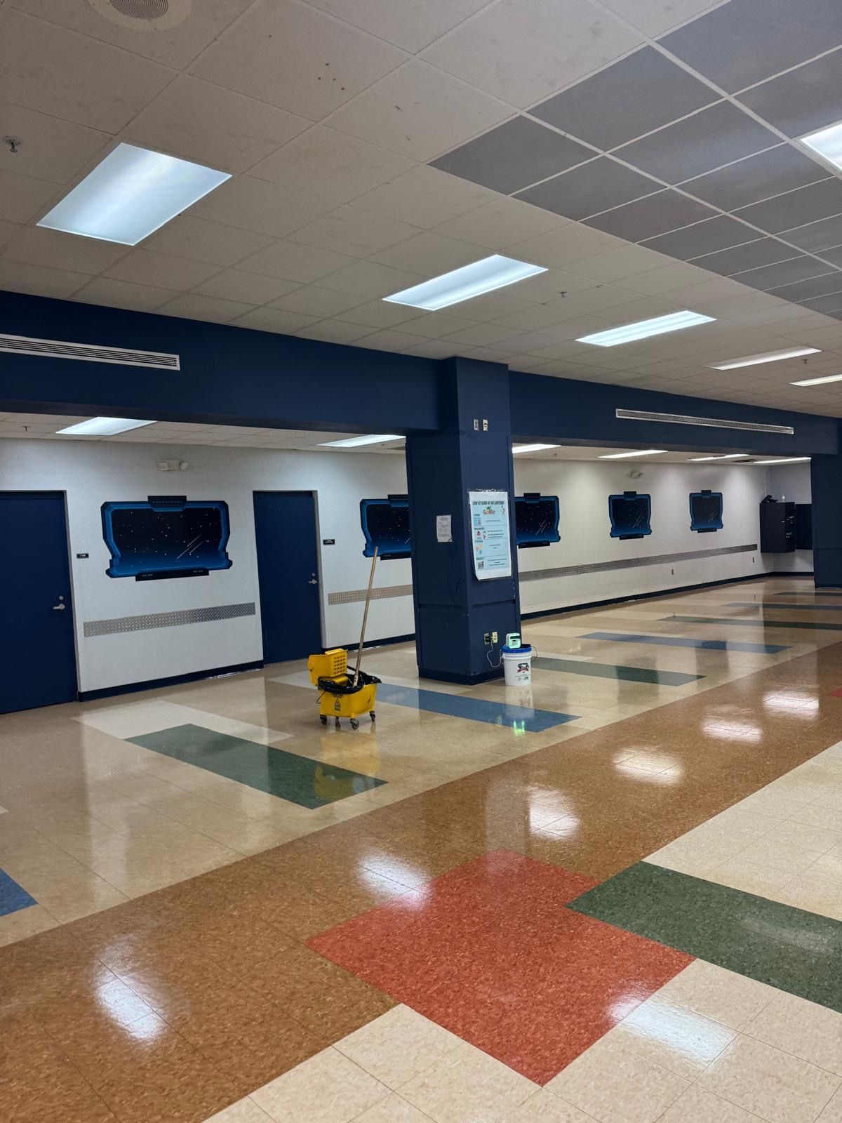 School hallway with mop bucket and blue walls, tiled floor.