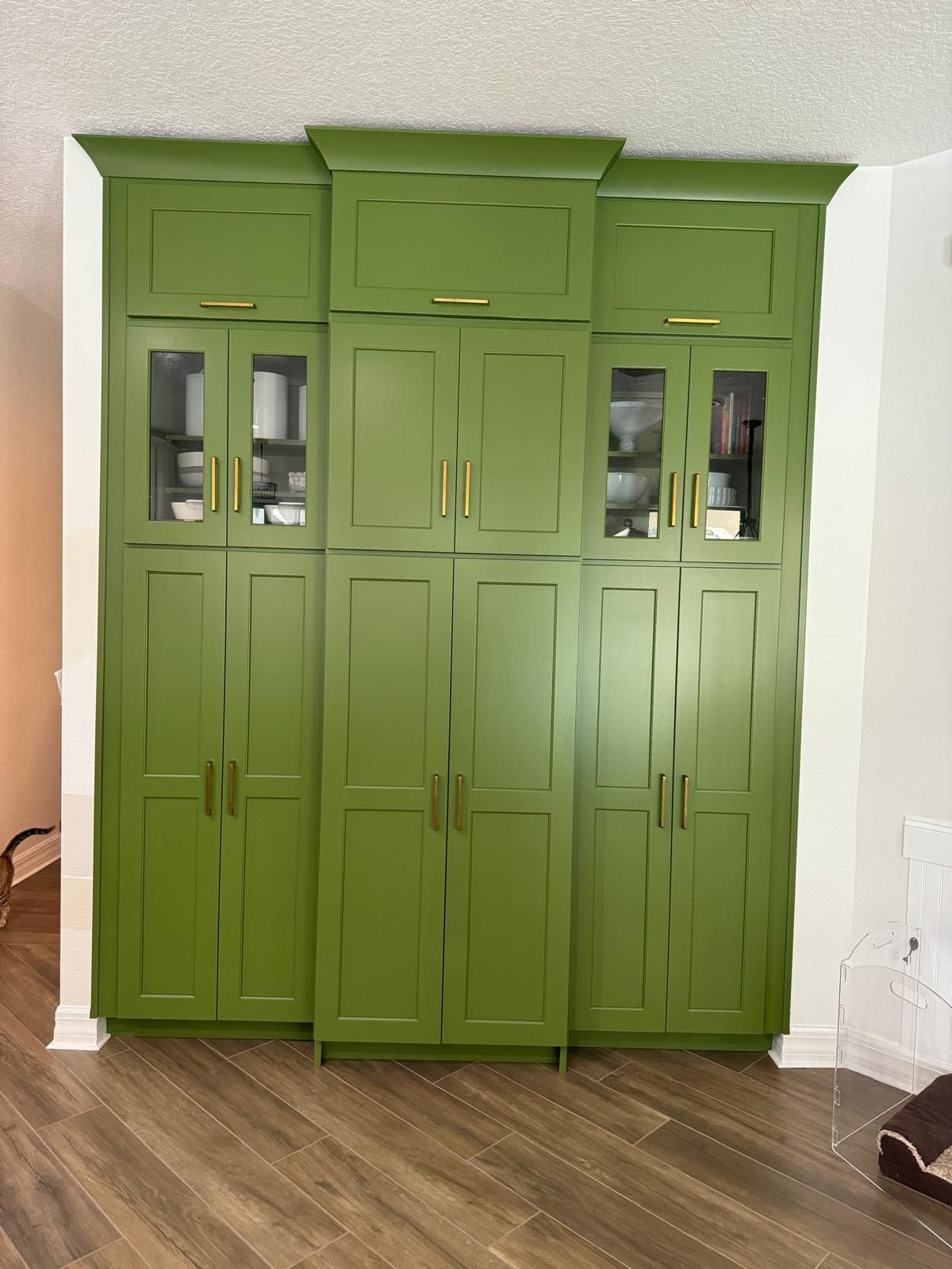 Green kitchen cabinets with gold hardware against a white wall.