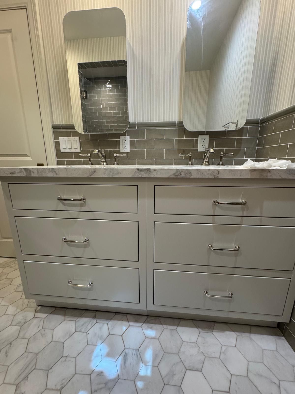 Bathroom vanity with gray cabinets, marble countertop, and hexagon tile floor. Two mirrors and sinks.