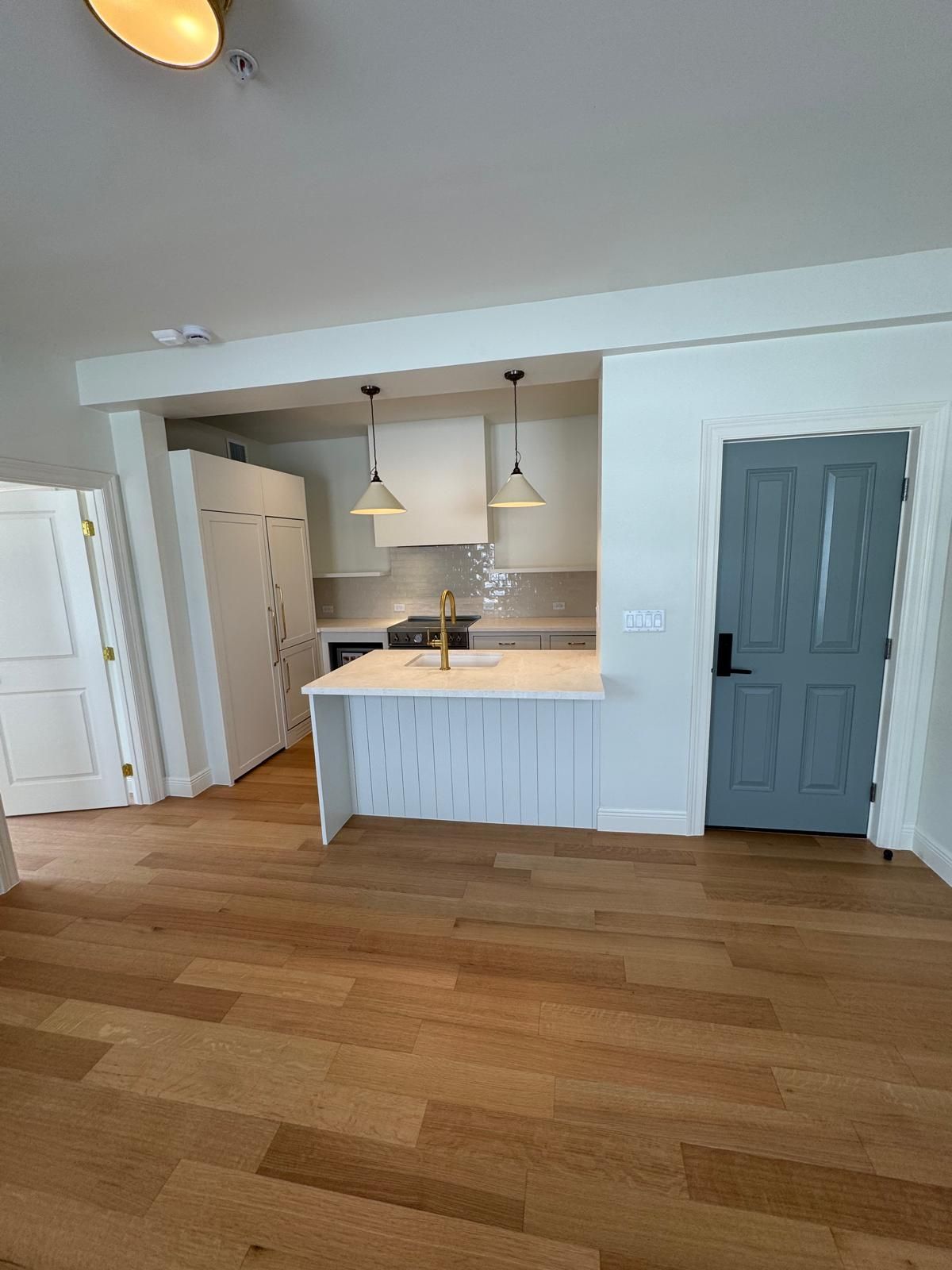 Open kitchen with light wood floors, white cabinets, and a gray door.