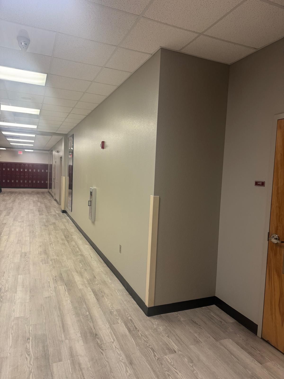 School hallway with gray walls and flooring, red lockers, and a closed brown door.