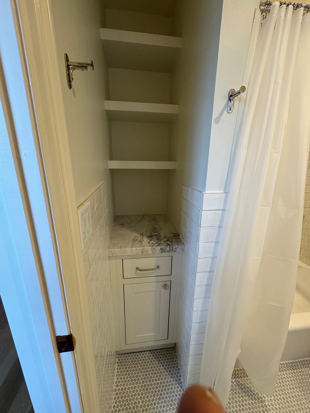 Bathroom niche with white shelves, cabinet, and tile. Shower curtain on the right.