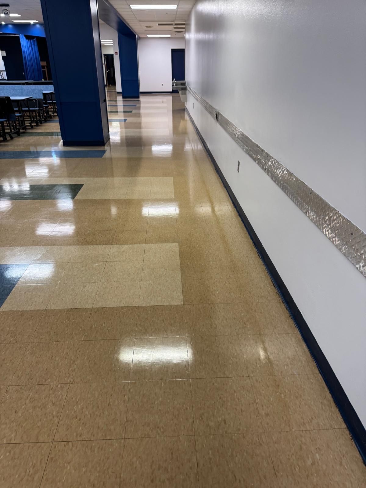 Long school hallway with tiled floors, white walls, and blue accents.