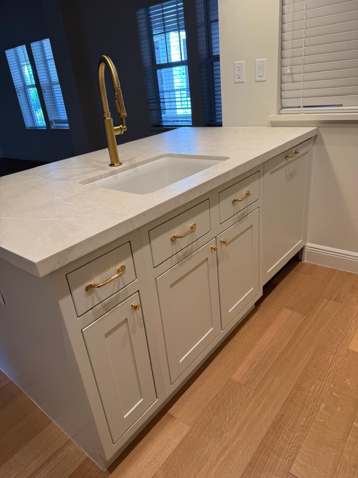 White kitchen island with a gold faucet and hardware. Wood floor and windows in the background.