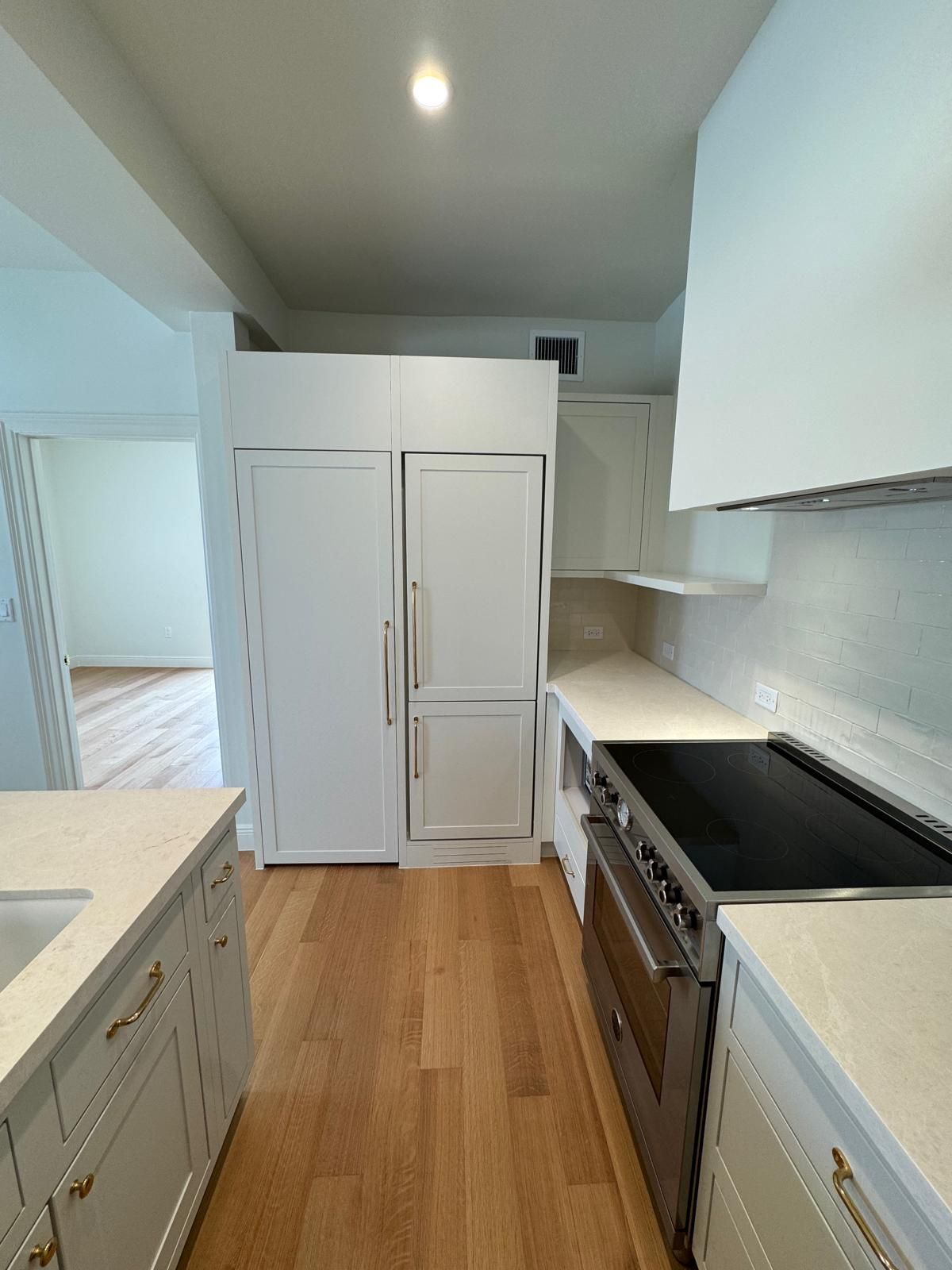 White kitchen with refrigerator, stove, and cabinets. Light wood floor.