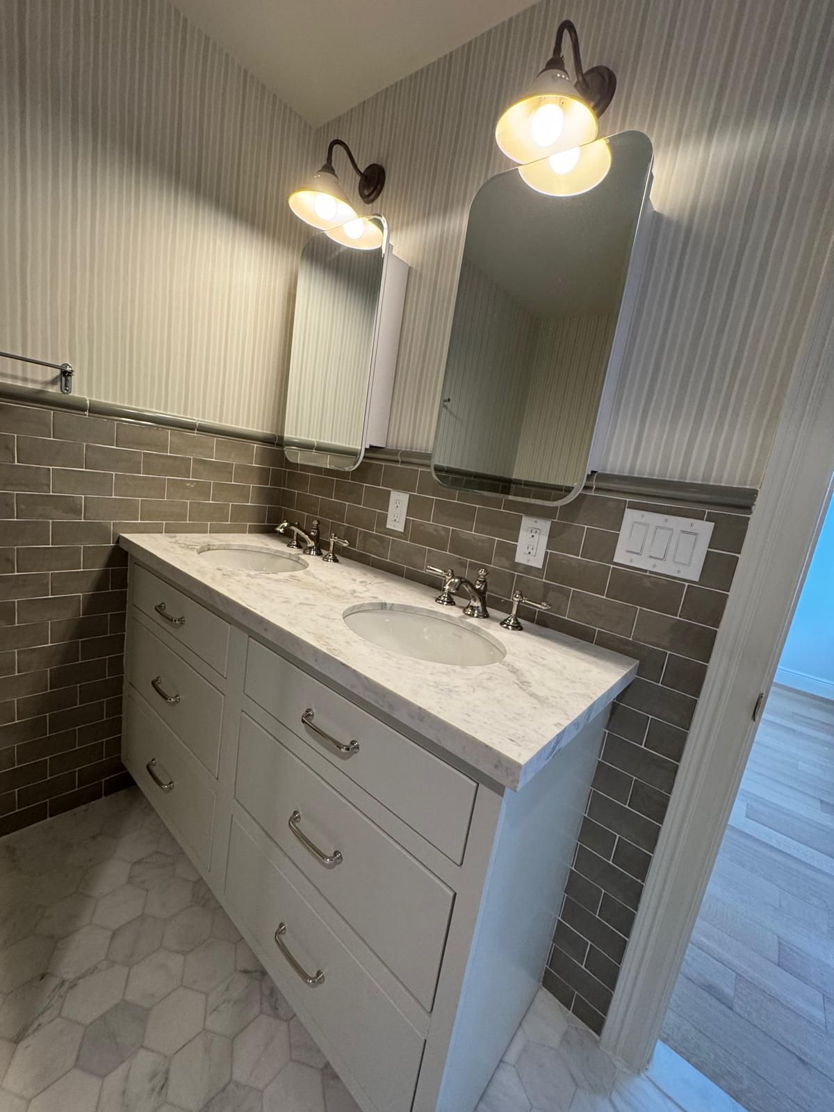 Bathroom vanity with two sinks, mirrors, and sconces; white cabinets, marble countertop, gray tile backsplash.