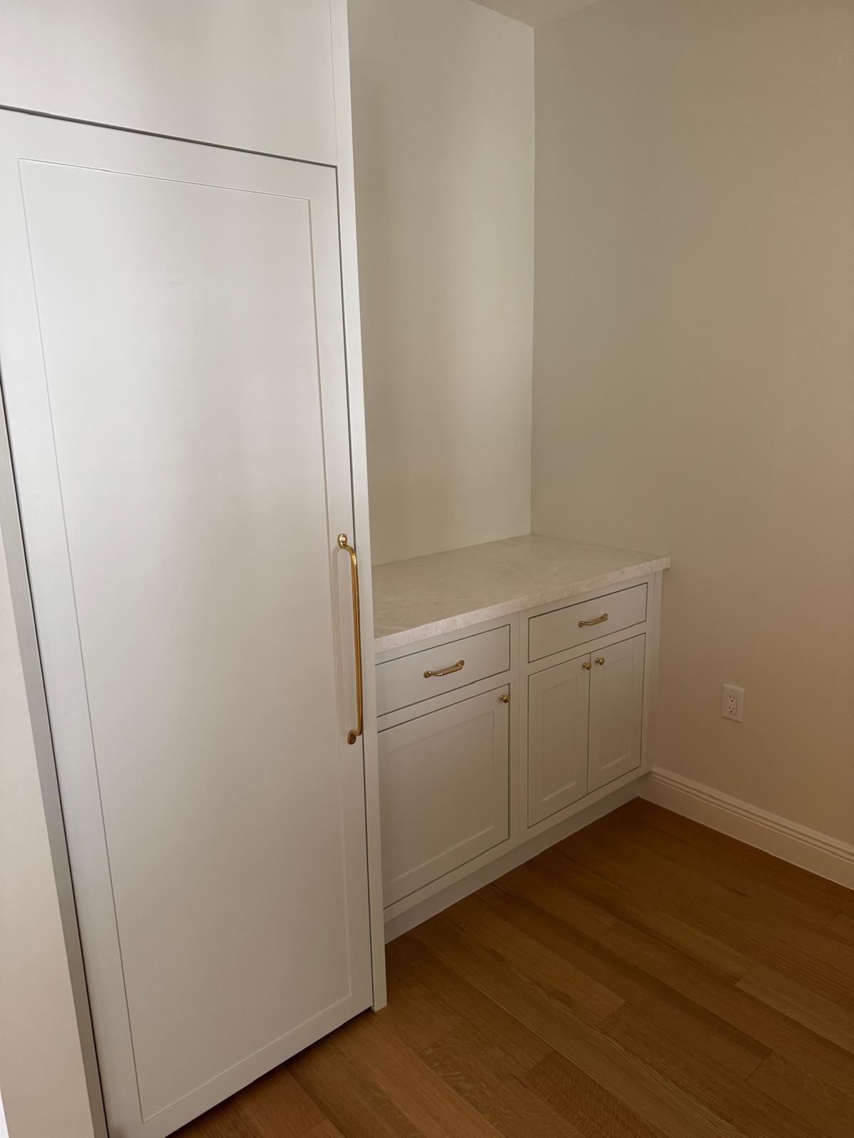 White built-in storage with countertop and a tall cabinet in a room with wood flooring and white walls.