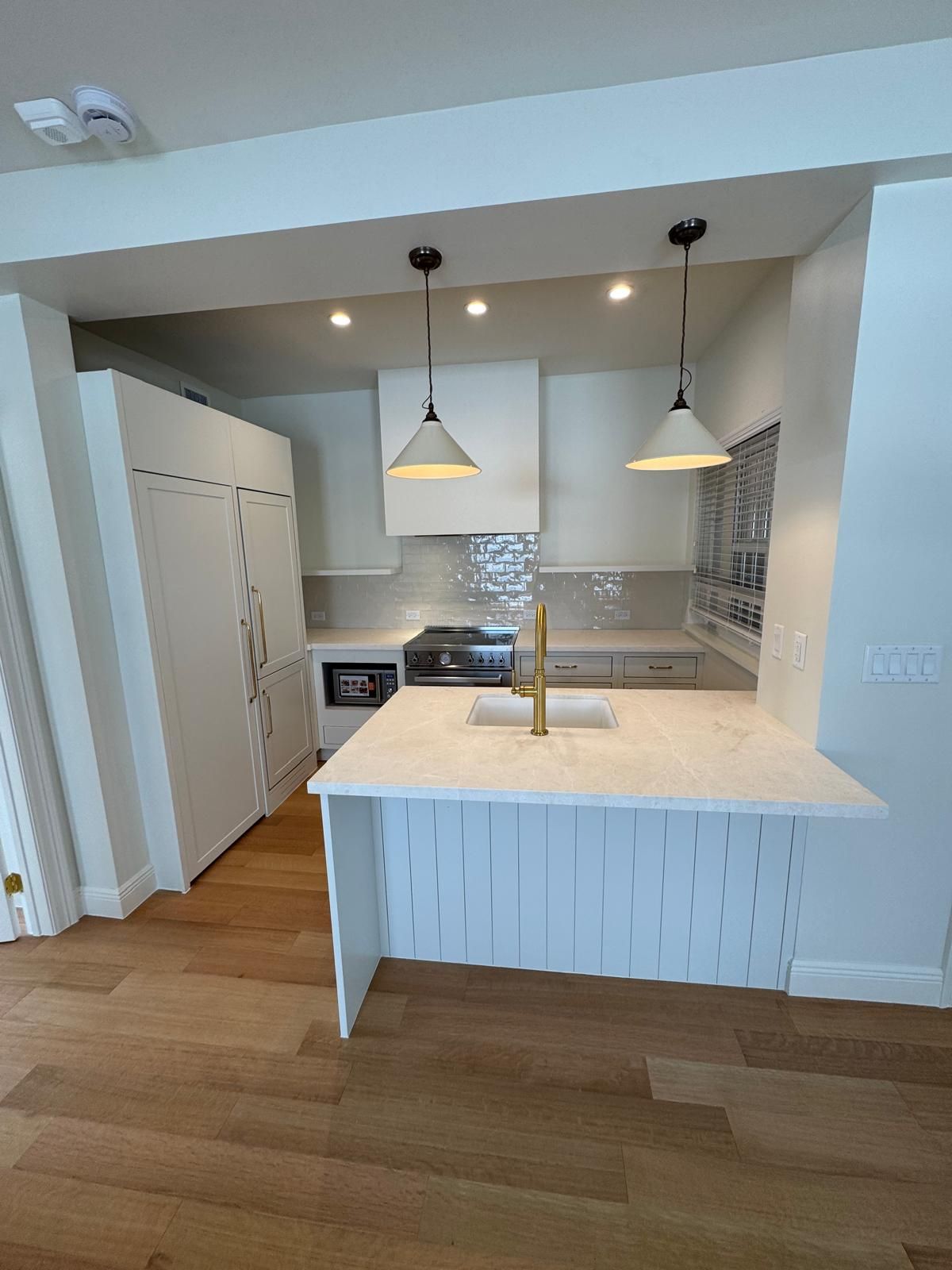 Modern white kitchen with island, pendant lights, and wood flooring.