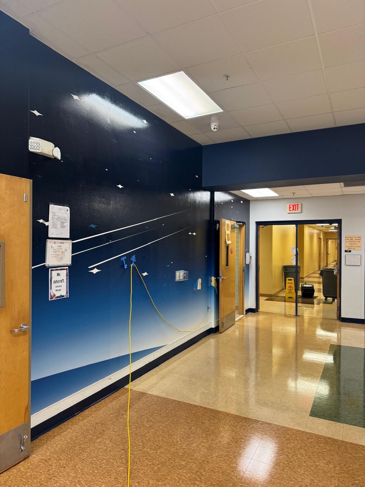 Hallway with a space mural on the left wall. Doorways and fluorescent lighting.