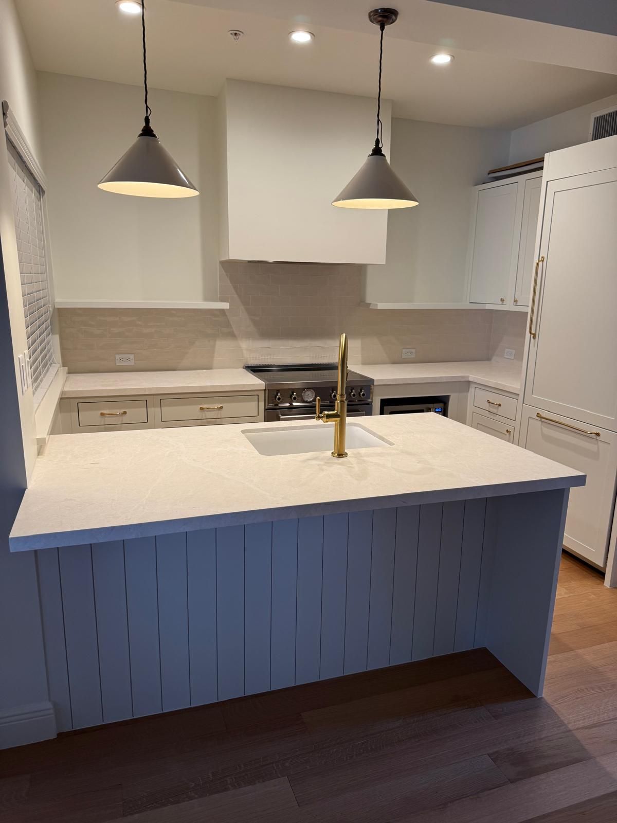 Modern white kitchen with island, pendant lights, gold faucet, and wooden floors.