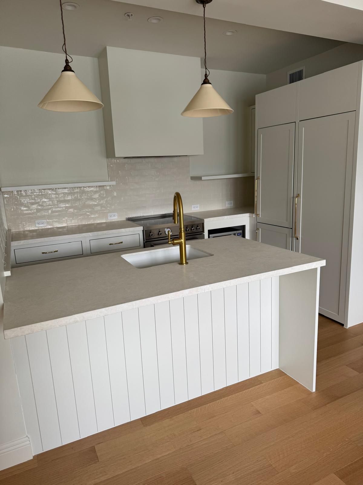 Modern white kitchen with island, gold faucet, pendant lights, and stainless steel appliances.