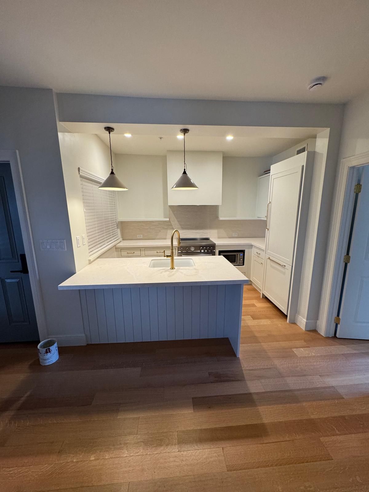 Modern kitchen with white cabinets, gold faucet, and pendant lights. Hardwood floors.