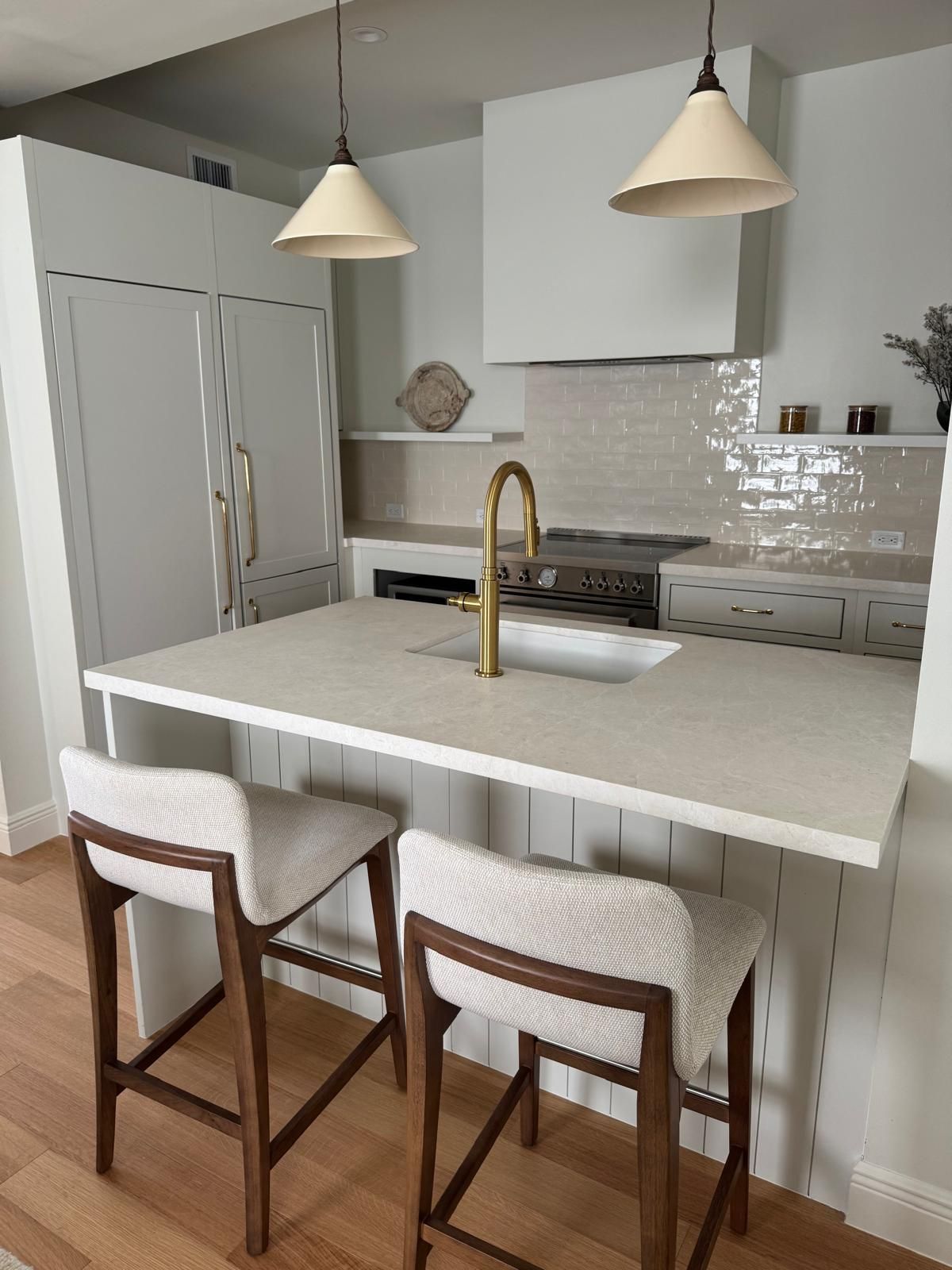 A modern kitchen with a breakfast bar, two stools, gold faucet, and white cabinets.