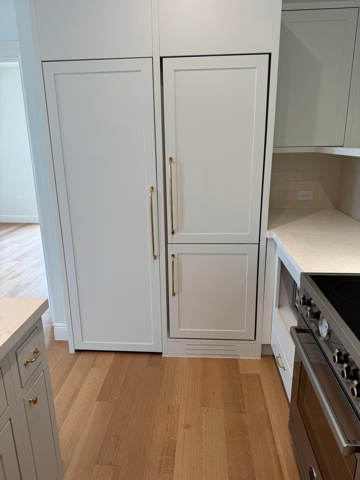 White built-in refrigerator and freezer in a kitchen with light wood floors.