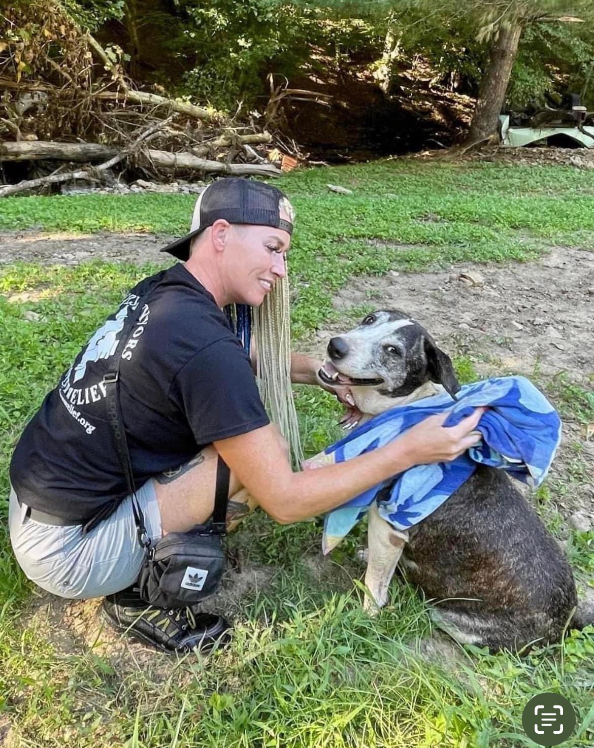 A man is kneeling down next to a dog wearing a blue towel.