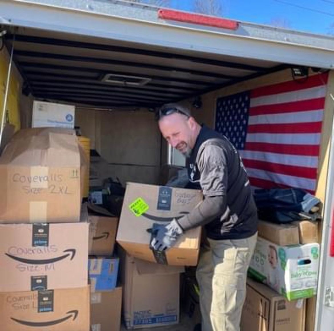 A man is carrying a box in a truck that has boxes stacked on top of each other