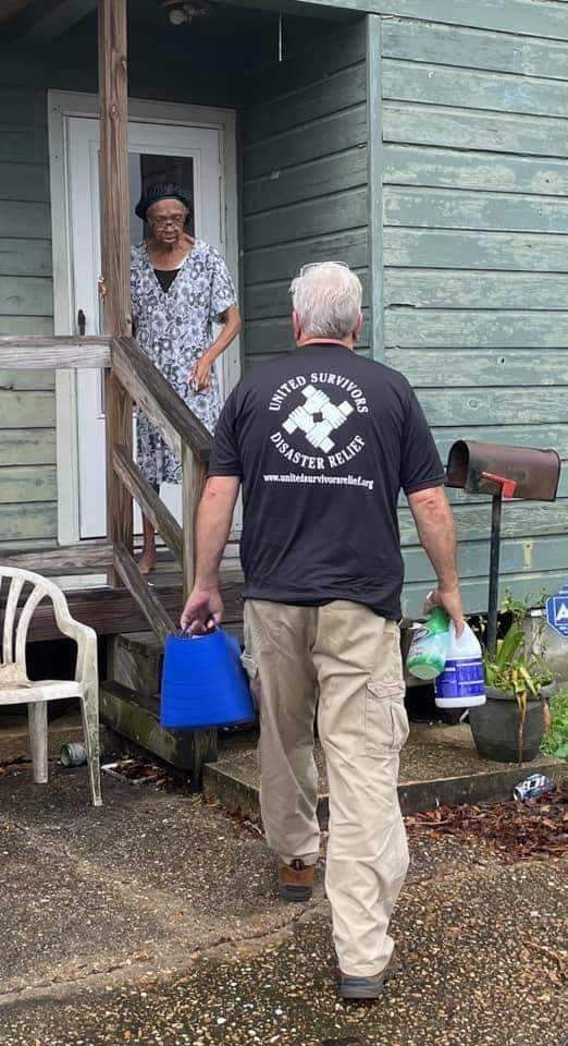 A man is carrying a bucket of water to a woman on the porch of a house.
