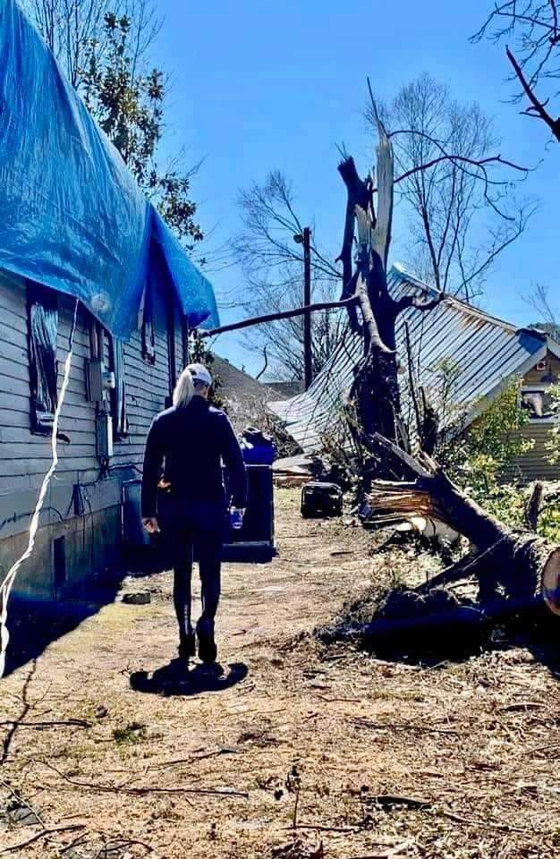 A man is standing in front of a house that has been damaged by a tornado.