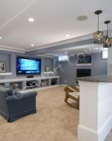A spacious, well-lit basement entertainment room with a TV, fireplace, and bar area.