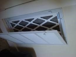 A rectangular air vent with a filter being accessed, built into a white wall.