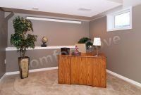 A home office with a wooden desk, large potted plant, and a small window on a beige carpet.