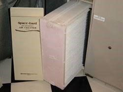 Space-Gard air cleaner filter and housing next to a furnace. White and tan colors.
