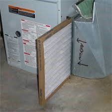 Air filter being replaced in a home's HVAC system. New filter in brown frame, ventilation duct on the right.