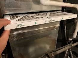 Hand holding a dirty furnace filter, showing its dimension: 16x20x1. The filter is being replaced.