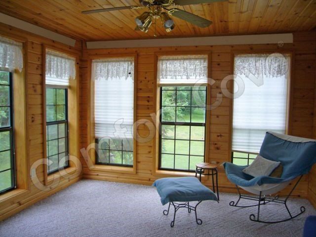 Sunroom with wooden walls, windows, a blue rocking chair, and white blinds.
