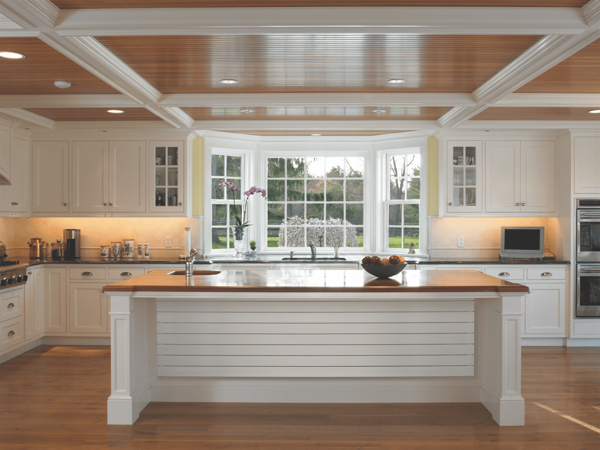 Bright white kitchen with a wooden island and ceiling, large window overlooking a garden.