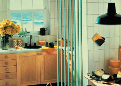 Kitchen scene with yellow flowers, wooden cabinets, a black sink, and vertical green strips partially obscuring the view.