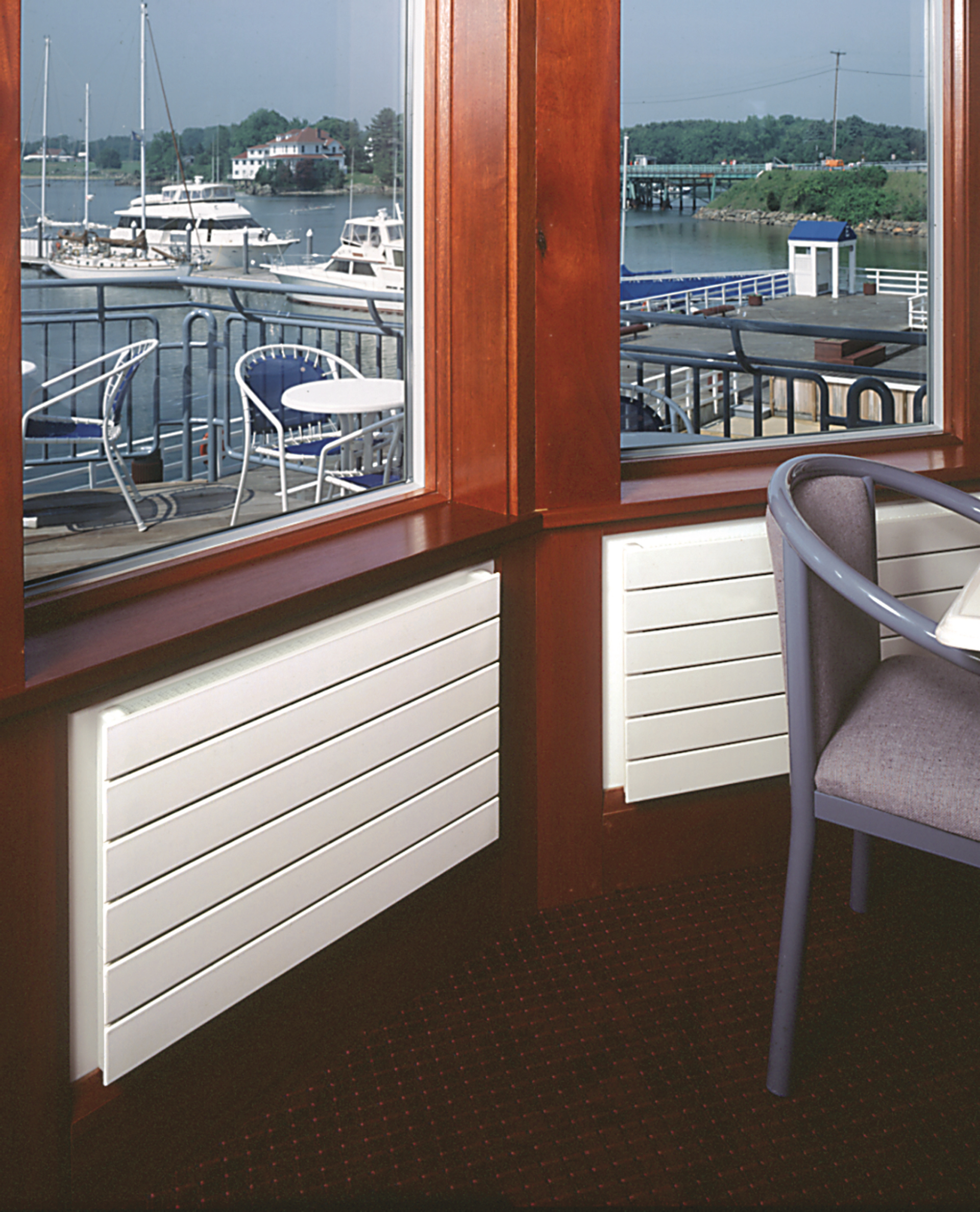 White heaters under windows with a view of a marina and boats.