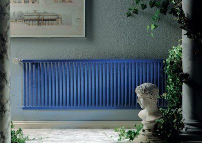 Blue radiator on a gray wall, with a bust, greenery, and classical columns.