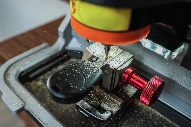 A key cutting machine carving a key; sawdust is visible.