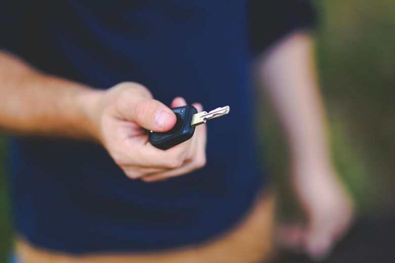 Person holding out a black car key, blurred background.