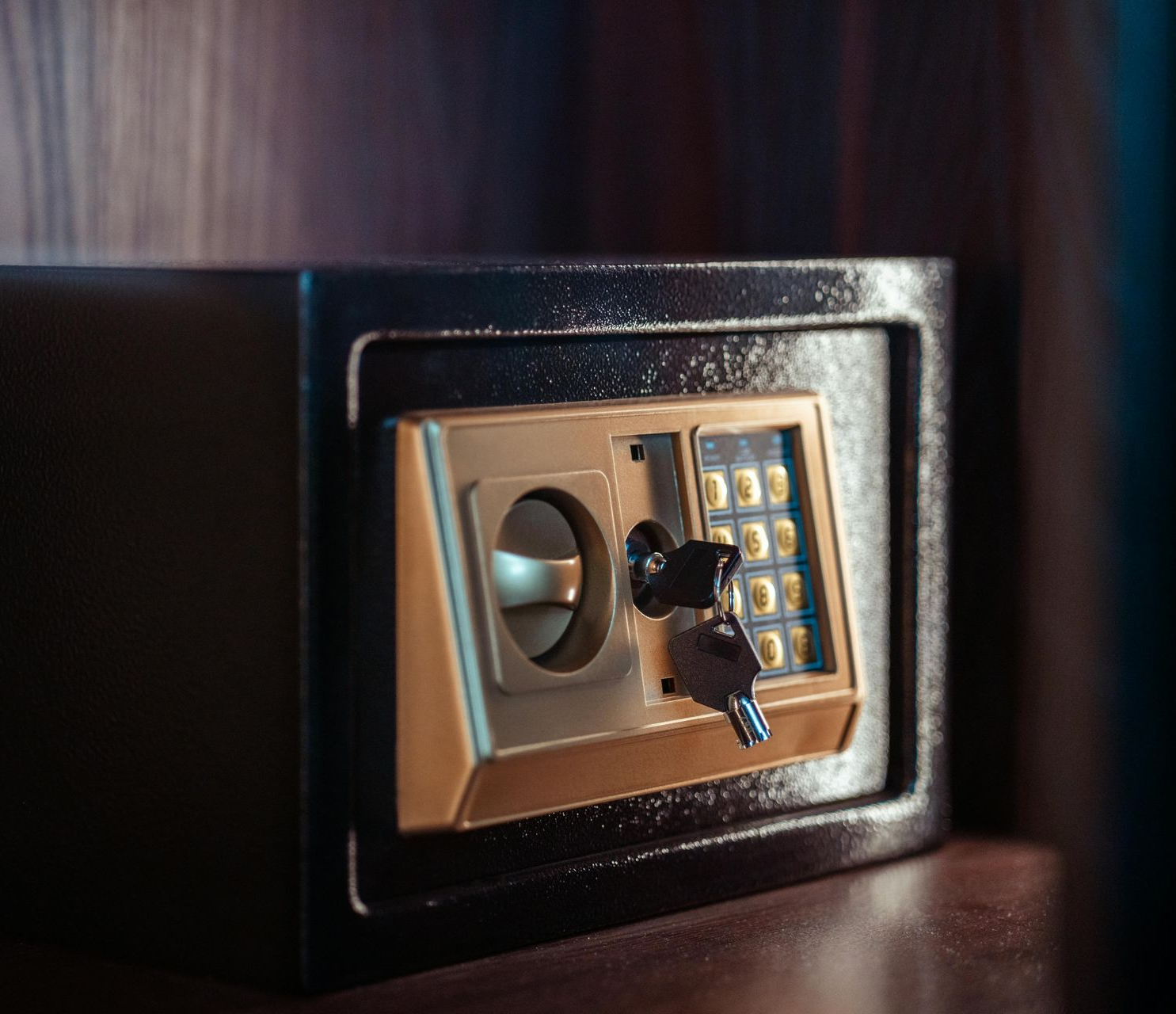 Black and gold safe with keypad and key in the lock, sitting on a wooden surface.