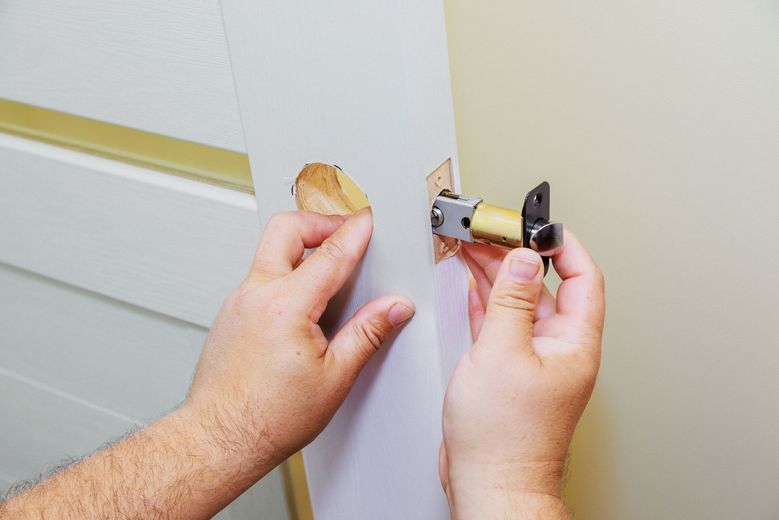 Hands holding a door latch mechanism, damaged door with paint peeling.