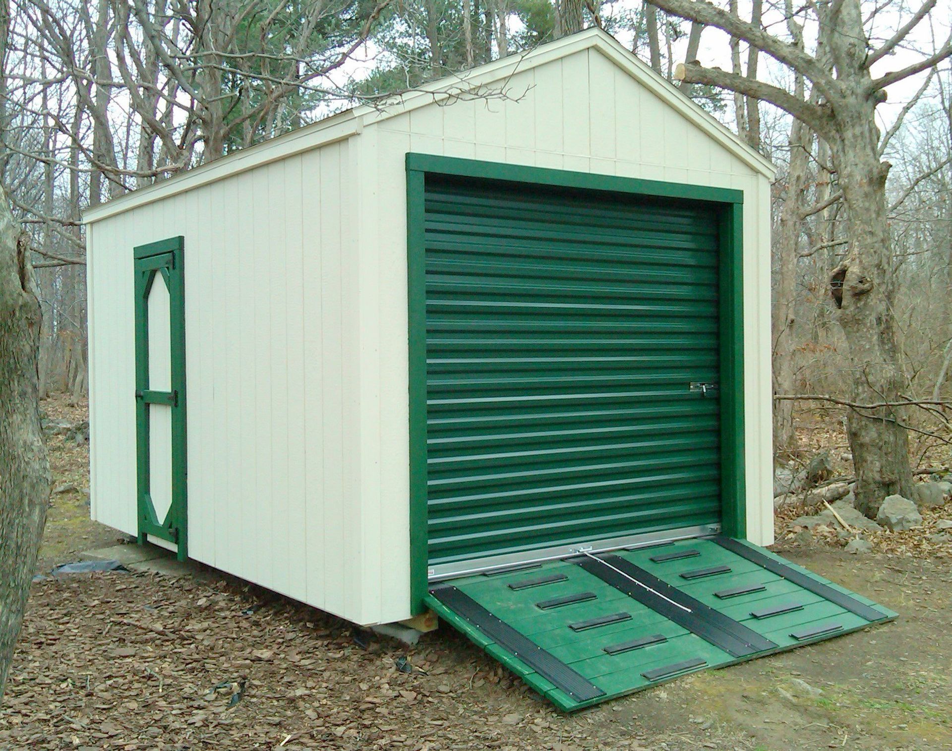 Green and white shed with a roll-up door, ramp, and an additional door on the side.